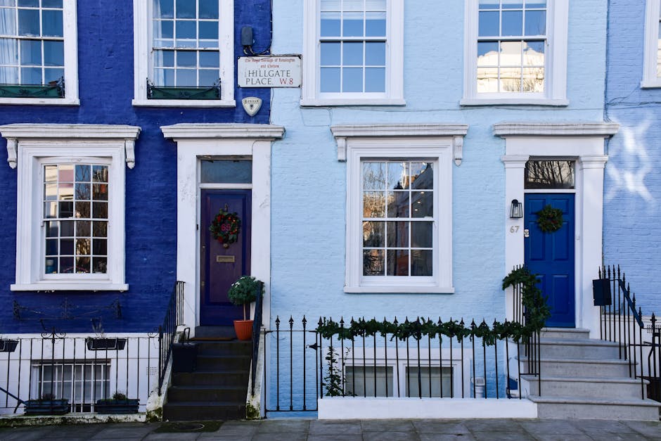 The image shows a row of two neighbouring terraced houses with facades painted in shades of blue, located on Hillgate Place in Westminster. Each house features white-framed sash windows and a front do